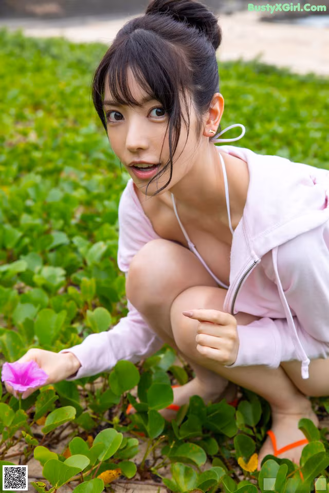 A woman crouching down with a flower in her hand.