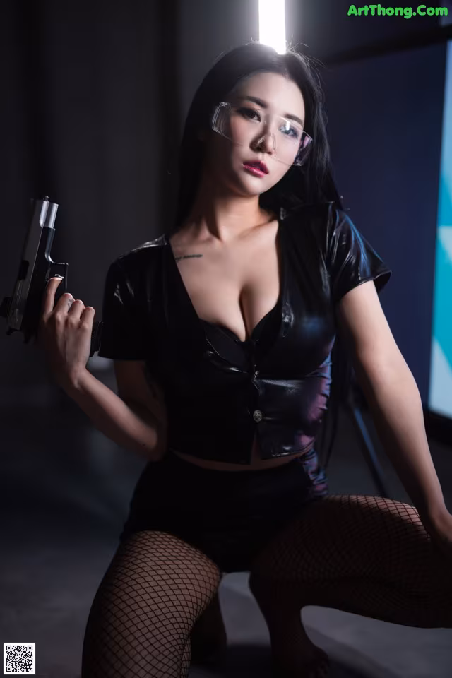 A woman in a black leather outfit holding a gun.