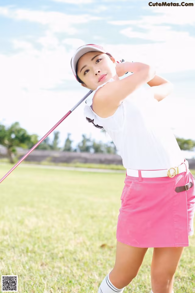 A woman in a pink skirt swinging a golf club.