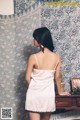 A woman standing in front of a dresser wearing a pink dress.