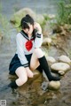 A woman in a school uniform sitting on a rock in the water.