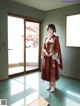 A woman in a red kimono standing in front of a window.