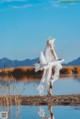 A woman in a white dress standing by a body of water.