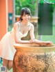 A woman in a white dress leaning on a large pot.