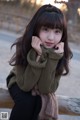 A young woman sitting on a wooden bench with her hand on her chin.