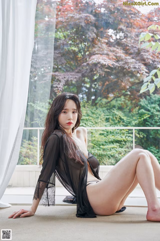 A woman sitting on the floor in front of a window.