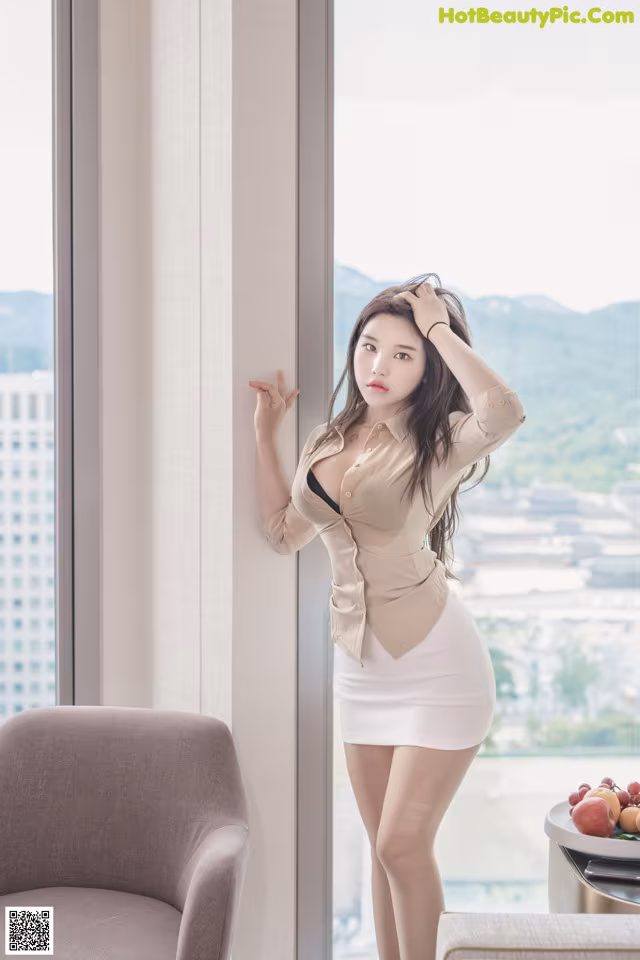A woman standing in front of a window next to a chair.