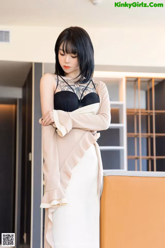 A woman in a black and white dress leaning against a wall.