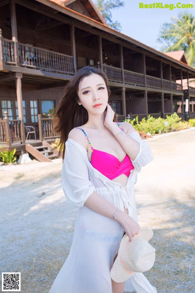 A woman in a white dress and a pink bikini posing for a picture.