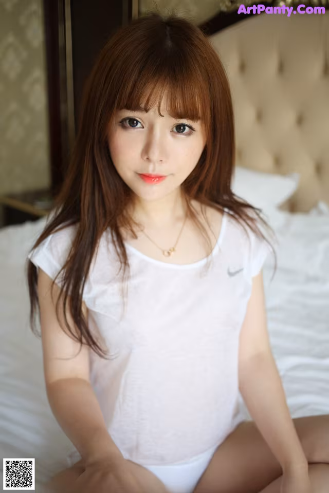 A woman sitting on top of a bed in a white shirt.