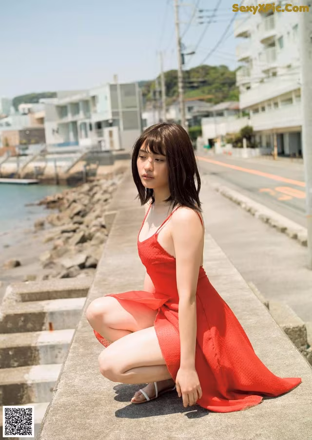 A woman in a red dress sitting on a concrete ledge.