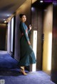 A woman in a long green dress standing in an elevator.