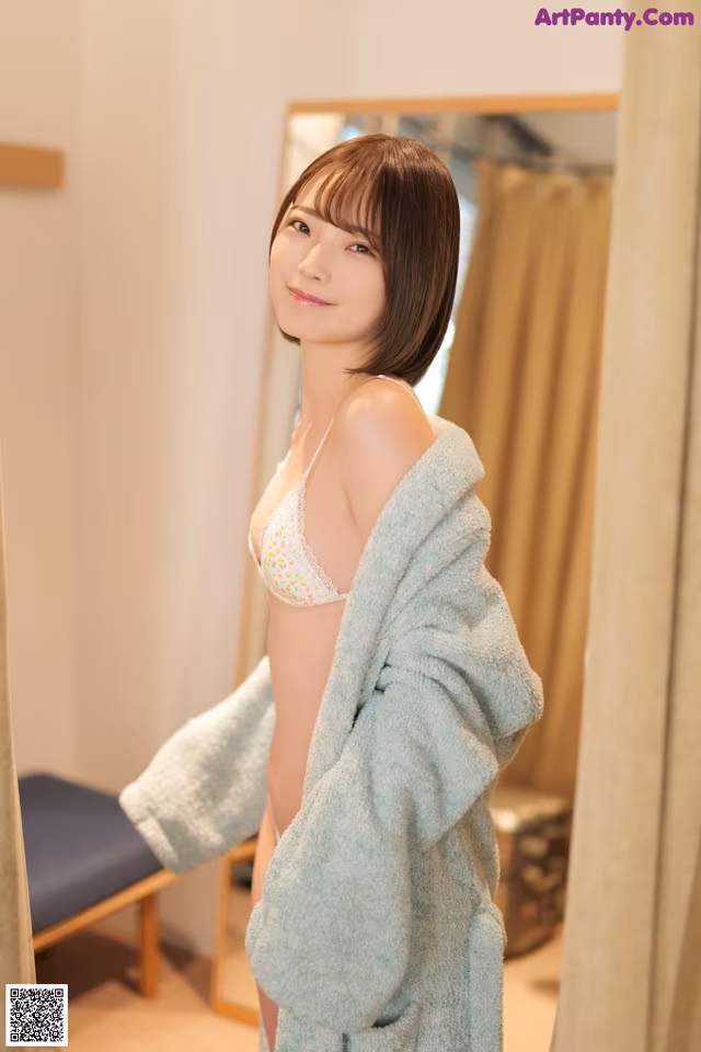 A woman in a blue robe standing in front of a mirror.
